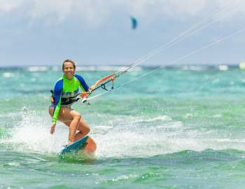 A woman kitesurfing smiles while she rides a wave onto shore